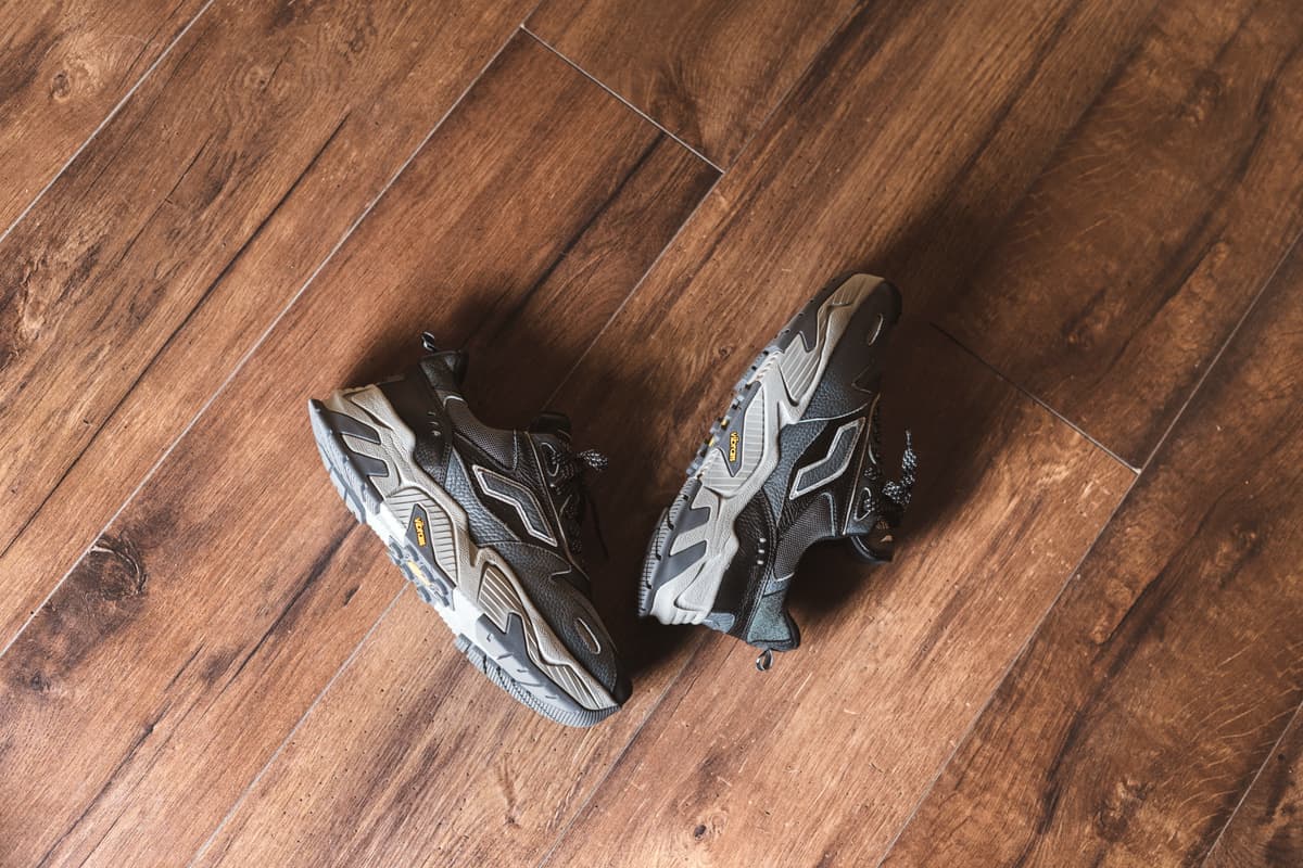 A pair of worn walking shoes on a hardwood floor beside a doorway